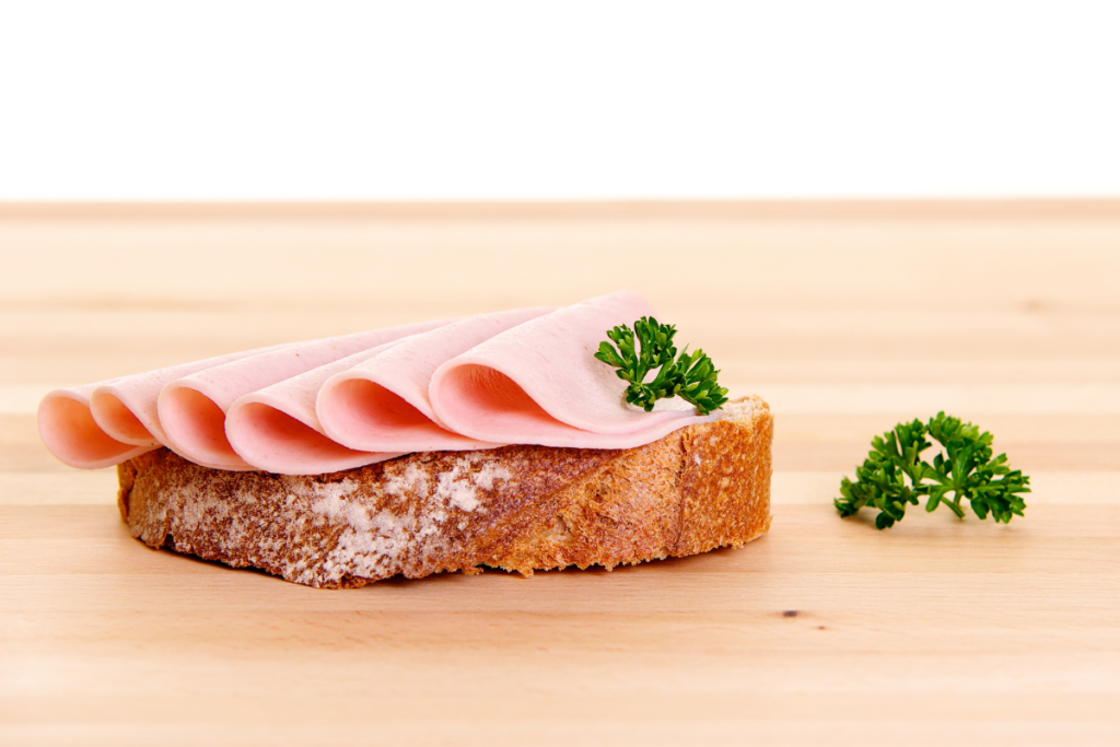 Pöydällä leipä, jonka päällä kinkkuviipaleita.
