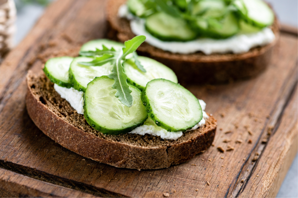 Leikkuulaudalla kaksi leipäviipaletta, joiden päällä raejuustoa ja kurkkua.