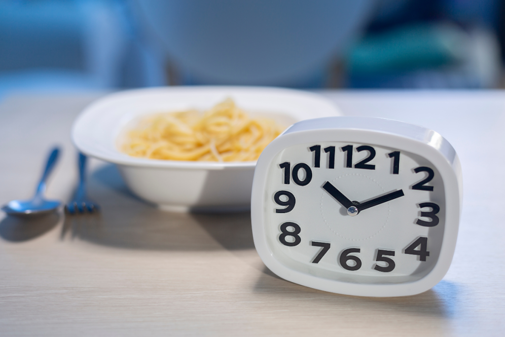 Kello, joka näyttää iltakymmentä. Taustalla lautasellinen pastaa. Myöhäinen syöminen.