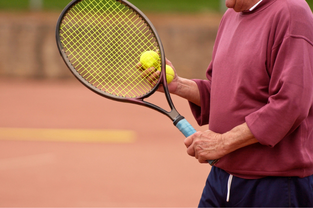 Lähikuva henkilöstä pitämässä tennismailaa ja palloa kädessä.