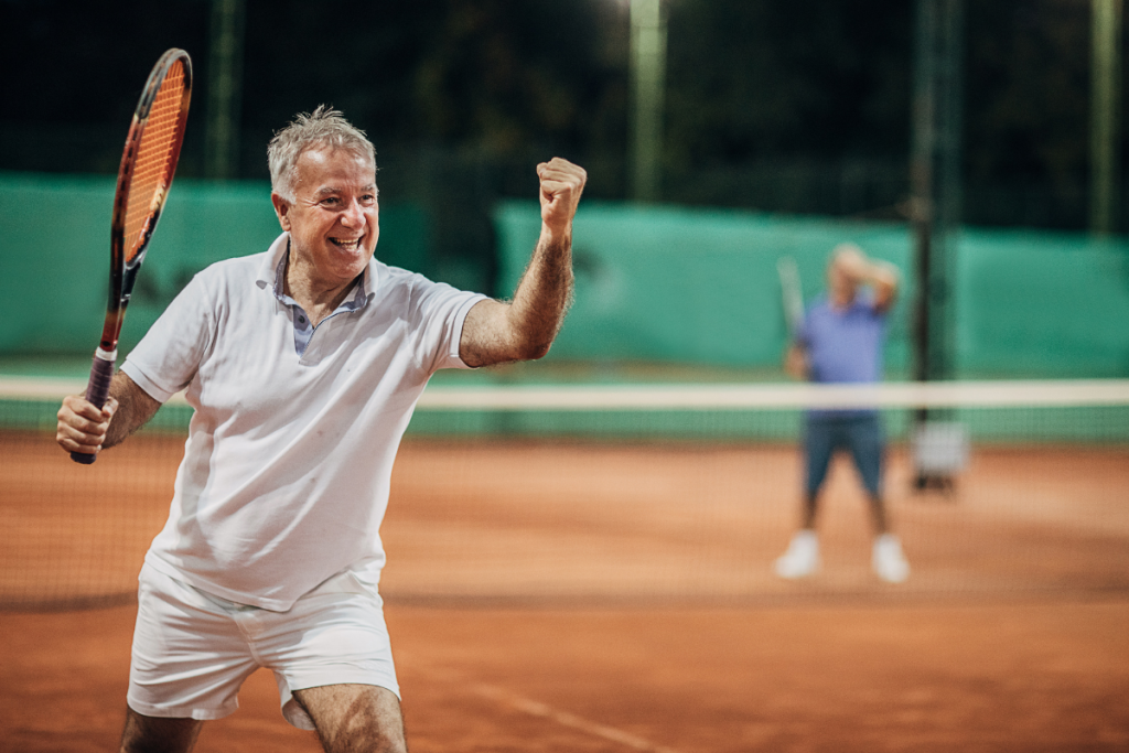Mies tuulettaa tenniskentällä maila kädessä.