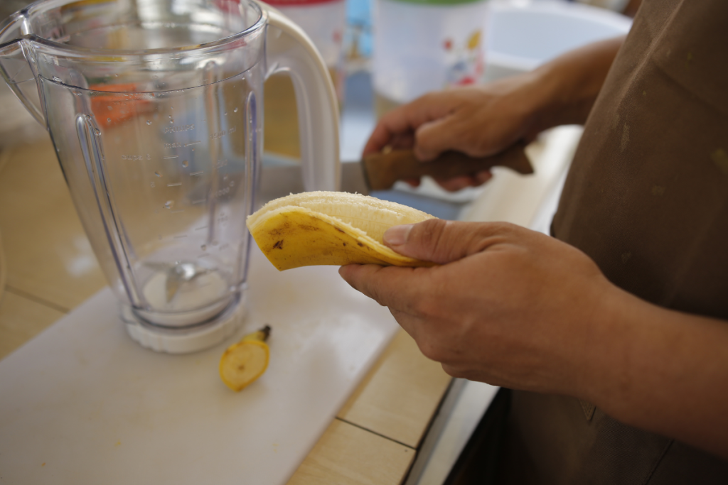 Henkilö kuorii banaania smoothieen.