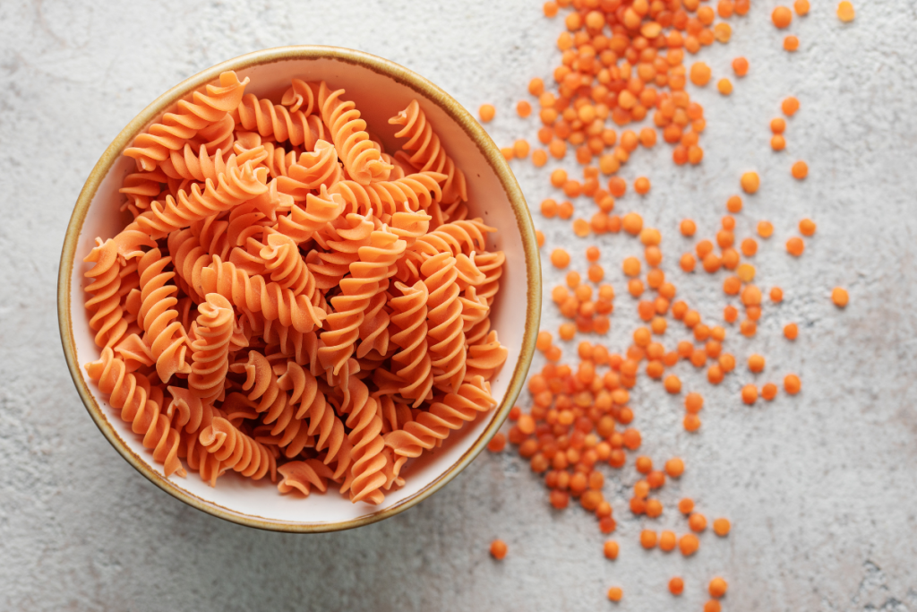 Oranssia linssipastaa kulhossa. Vieressä linssejä.